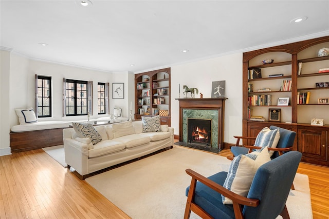 living room featuring a fireplace, crown molding, built in features, and light hardwood / wood-style floors