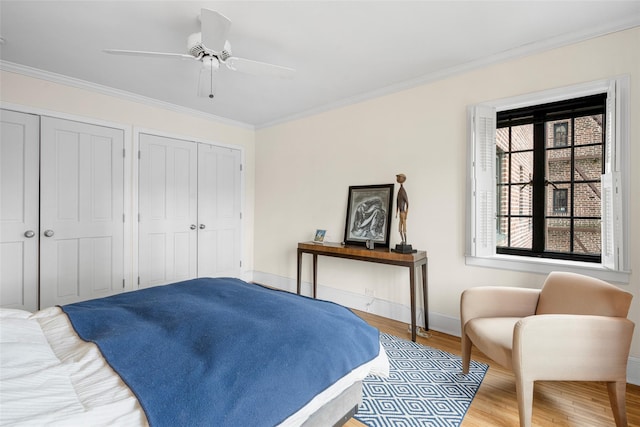 bedroom with two closets, ornamental molding, ceiling fan, and hardwood / wood-style flooring