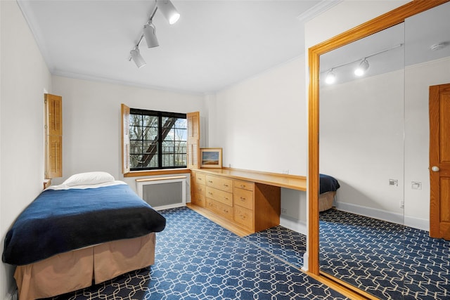 carpeted bedroom with built in desk, radiator heating unit, ornamental molding, and track lighting