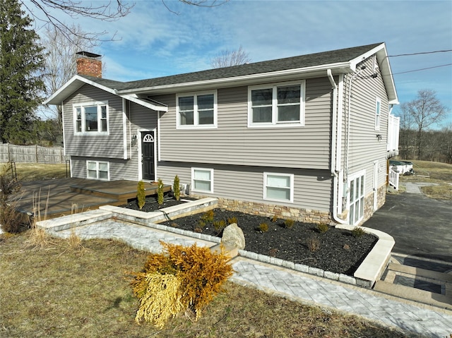 view of front of property featuring a chimney, a shingled roof, fence, a deck, and driveway