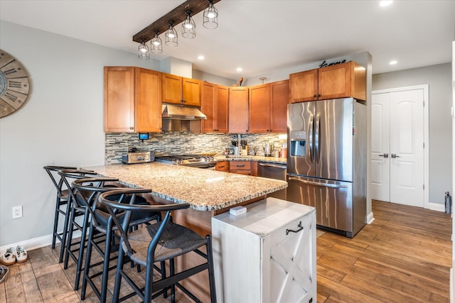 kitchen featuring a kitchen bar, light wood-type flooring, kitchen peninsula, stainless steel appliances, and decorative backsplash