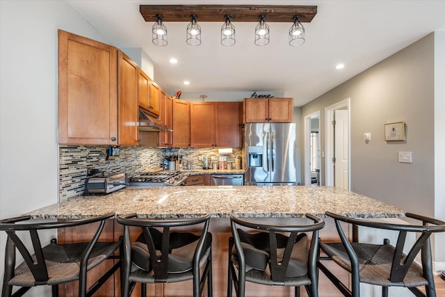 kitchen with appliances with stainless steel finishes, a breakfast bar area, backsplash, and kitchen peninsula