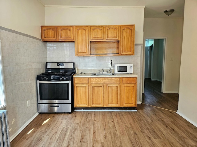 kitchen with stainless steel gas range oven, sink, radiator heating unit, and light hardwood / wood-style flooring