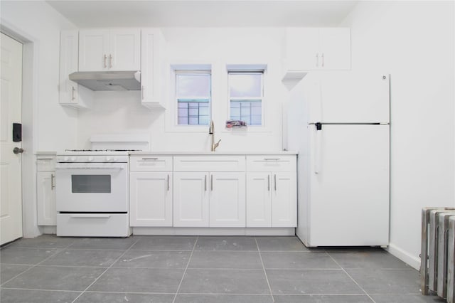 kitchen featuring sink, white appliances, dark tile patterned floors, radiator heating unit, and white cabinets