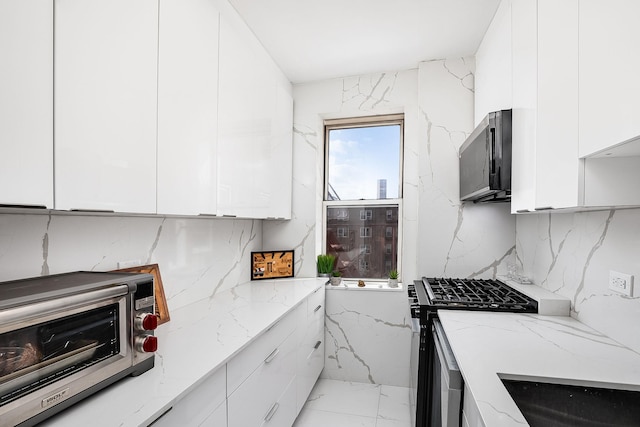 kitchen with tasteful backsplash, light stone countertops, appliances with stainless steel finishes, and white cabinets