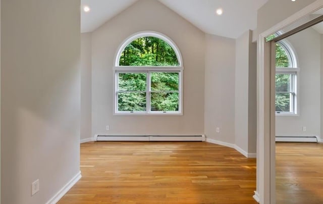 unfurnished room featuring baseboard heating, vaulted ceiling, and light hardwood / wood-style floors