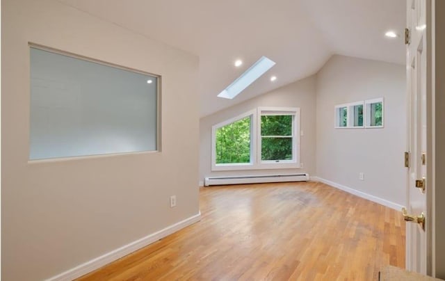 additional living space with a baseboard radiator, light hardwood / wood-style floors, and vaulted ceiling with skylight