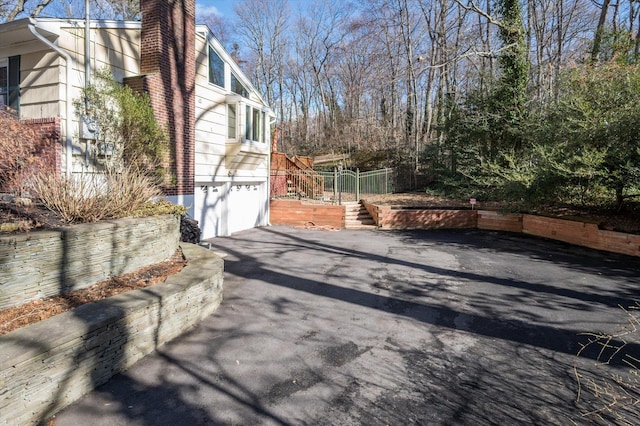 view of side of home with aphalt driveway, a chimney, an attached garage, and stairs