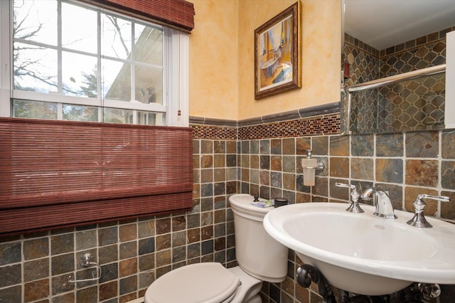 full bath with toilet, a wainscoted wall, a shower with door, a sink, and tile walls