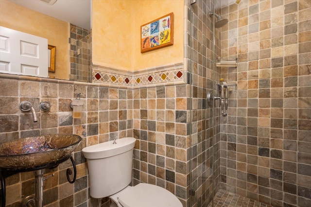 bathroom featuring a wainscoted wall, tile walls, toilet, a sink, and tiled shower