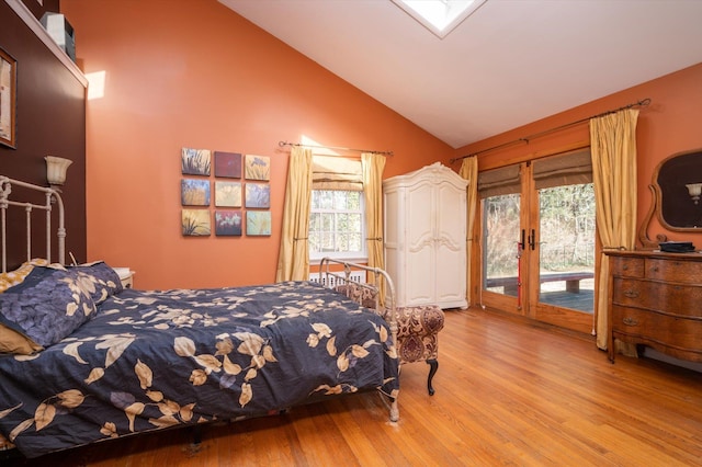 bedroom with access to outside, light wood finished floors, a skylight, and high vaulted ceiling