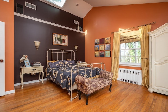 bedroom featuring radiator heating unit, lofted ceiling with skylight, and wood-type flooring