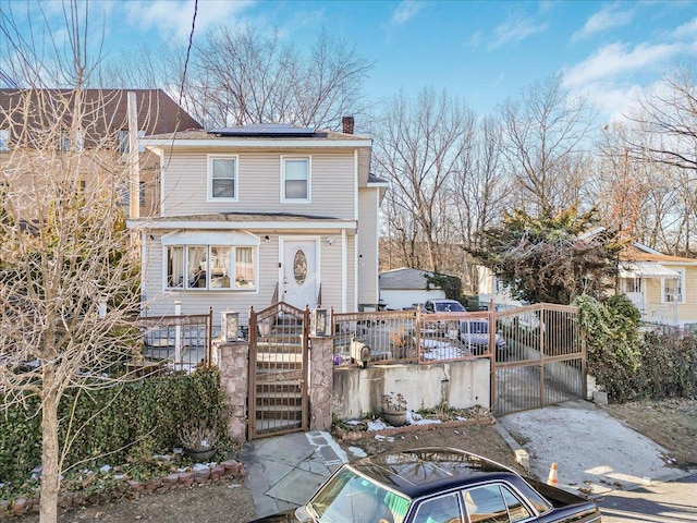 traditional style home featuring a fenced front yard, roof mounted solar panels, a chimney, and a gate