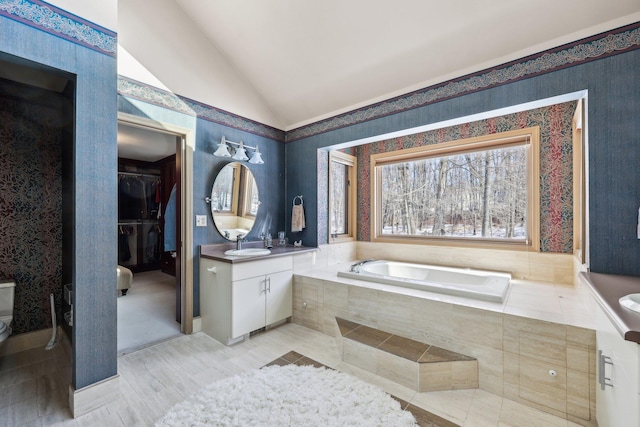 bathroom featuring tiled bath, vaulted ceiling, and vanity