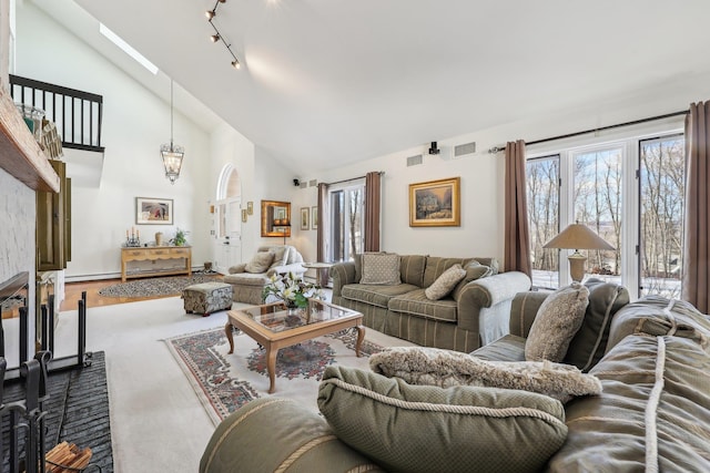 living room featuring high vaulted ceiling, a skylight, rail lighting, and a stone fireplace