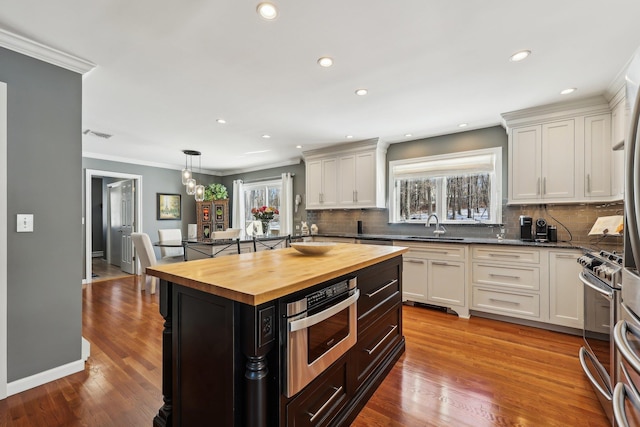 kitchen featuring white cabinets, wood counters, pendant lighting, stainless steel gas stove, and sink