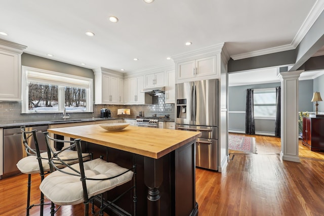 kitchen featuring appliances with stainless steel finishes, butcher block countertops, a kitchen island, white cabinetry, and decorative columns