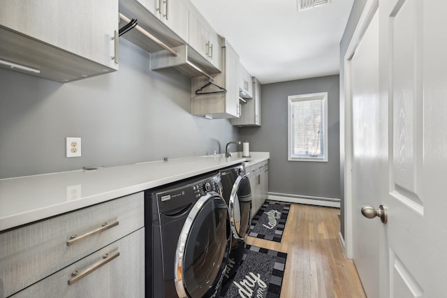 clothes washing area featuring sink, washer and clothes dryer, cabinets, light hardwood / wood-style floors, and a baseboard radiator