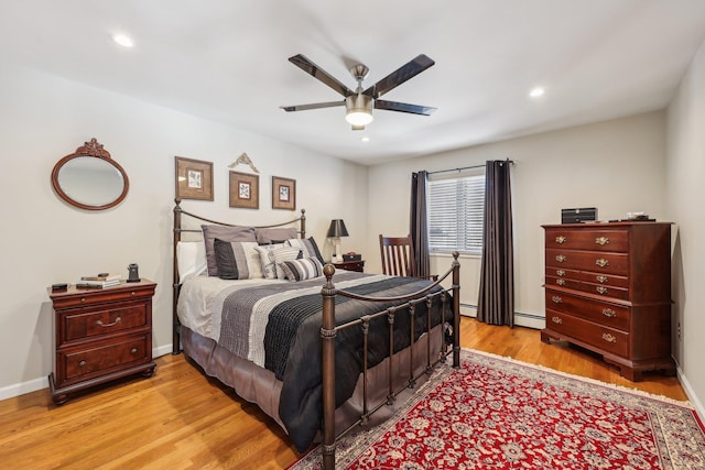 bedroom with light hardwood / wood-style floors, baseboard heating, and ceiling fan