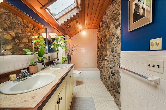 bathroom featuring tile patterned floors, toilet, tile walls, and lofted ceiling with skylight