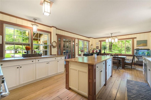 kitchen with crown molding, pendant lighting, white cabinets, and light wood-type flooring