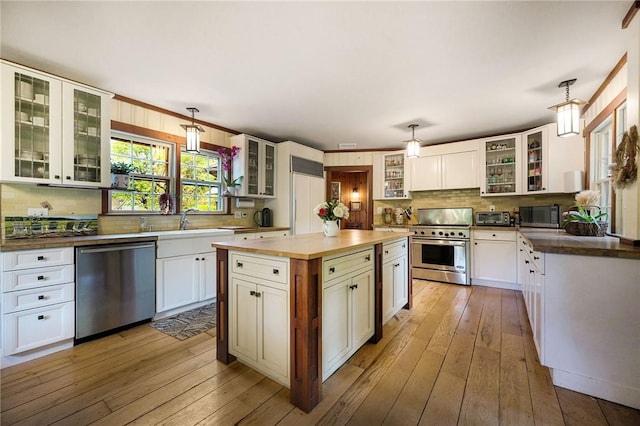 kitchen featuring white cabinetry, stainless steel appliances, hanging light fixtures, and light wood-type flooring