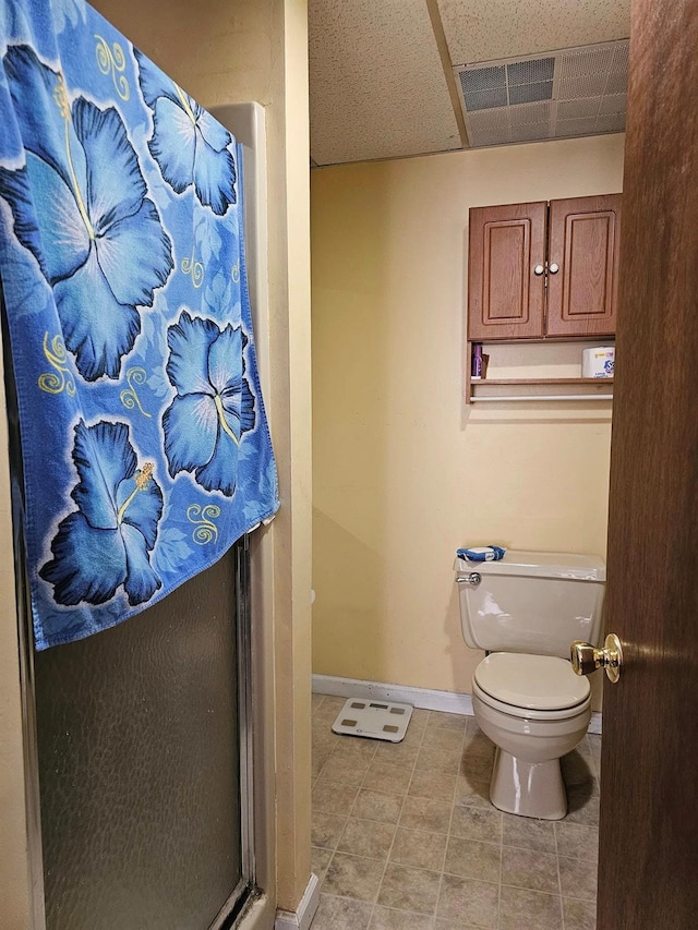 bathroom featuring a paneled ceiling, tile patterned floors, toilet, and a shower with shower door