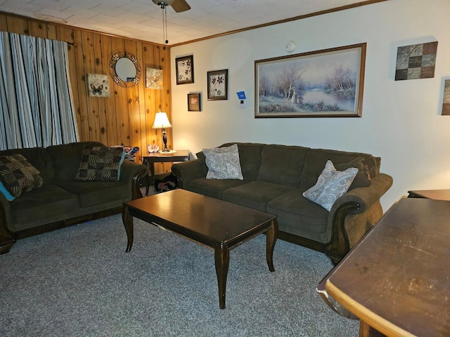 carpeted living room with crown molding, ceiling fan, and wood walls