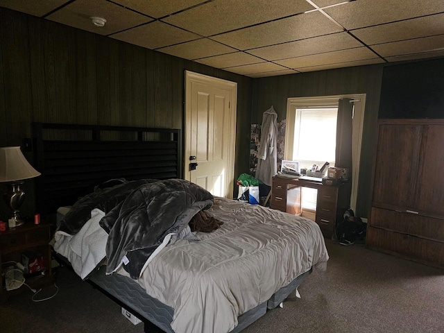 carpeted bedroom with a paneled ceiling and wood walls