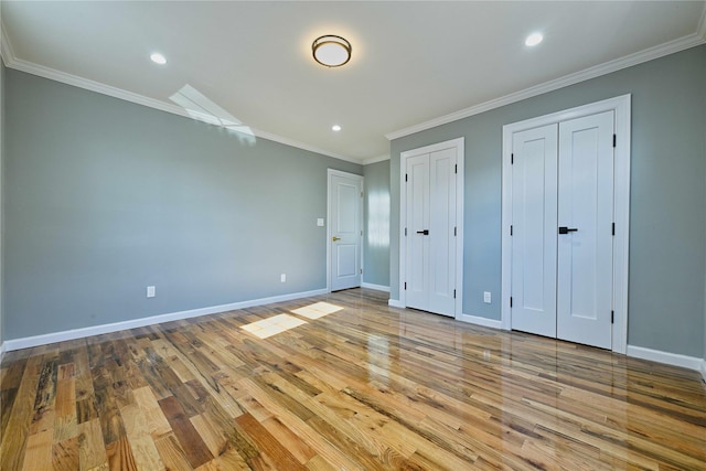 unfurnished bedroom featuring crown molding, two closets, and light hardwood / wood-style flooring