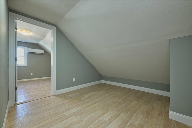 additional living space featuring vaulted ceiling, light hardwood / wood-style floors, an AC wall unit, and a textured ceiling