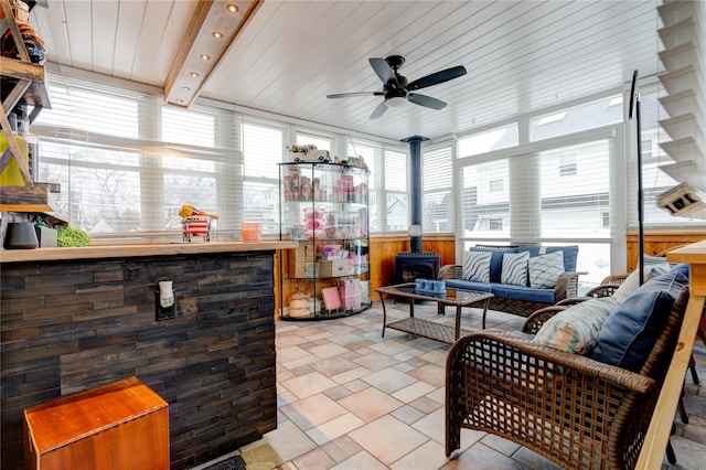 sunroom featuring a wealth of natural light, beamed ceiling, ceiling fan, and a wood stove