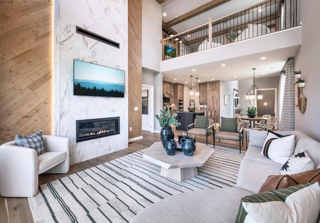 living room featuring wood finished floors, an inviting chandelier, a high ceiling, a fireplace, and recessed lighting