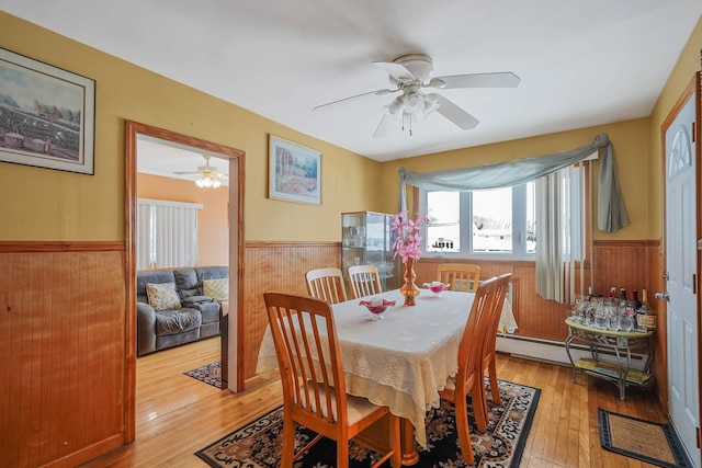 dining area with a baseboard heating unit, wood walls, ceiling fan, and light hardwood / wood-style flooring