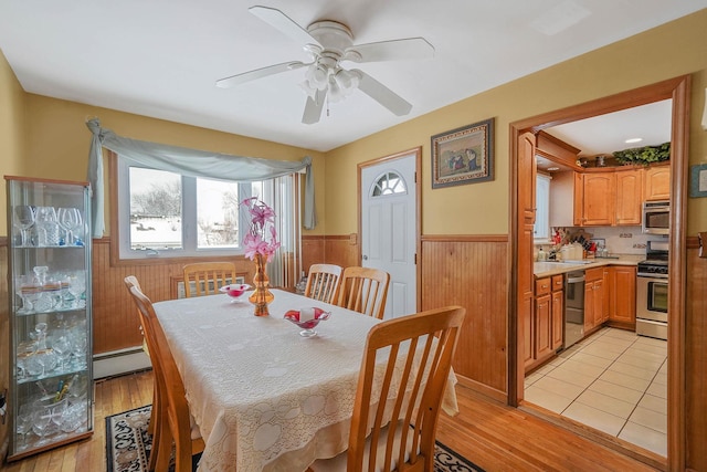 dining room featuring a baseboard heating unit, light hardwood / wood-style floors, ceiling fan, and wood walls