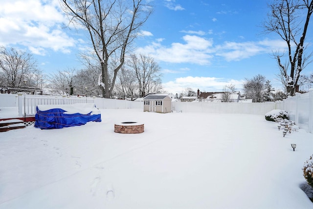 yard covered in snow with a shed, a swimming pool, and an outdoor fire pit