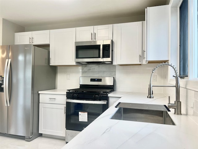 kitchen with appliances with stainless steel finishes, tasteful backsplash, white cabinetry, sink, and light stone countertops