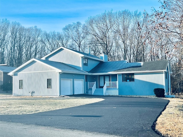 view of front of home with driveway, covered porch, a shingled roof, a garage, and a chimney