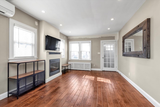 unfurnished living room with hardwood / wood-style floors, radiator, and a wall mounted air conditioner