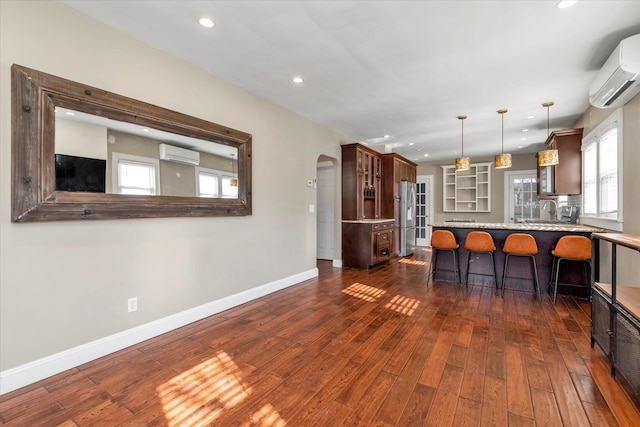 kitchen featuring an AC wall unit, stainless steel refrigerator, dark hardwood / wood-style flooring, kitchen peninsula, and pendant lighting