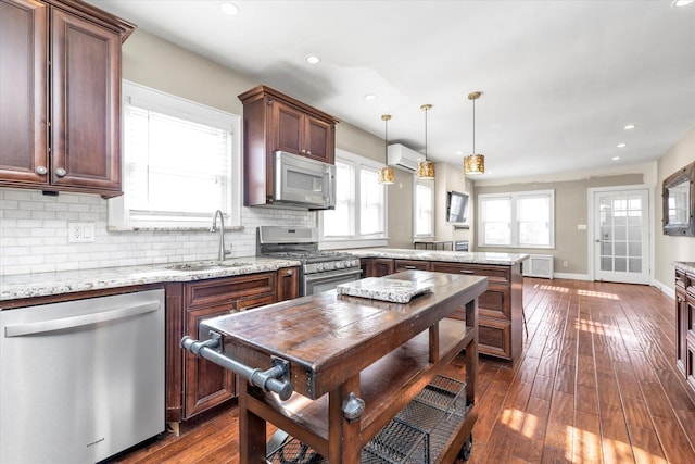 kitchen featuring radiator, a wall mounted air conditioner, sink, hanging light fixtures, and stainless steel appliances