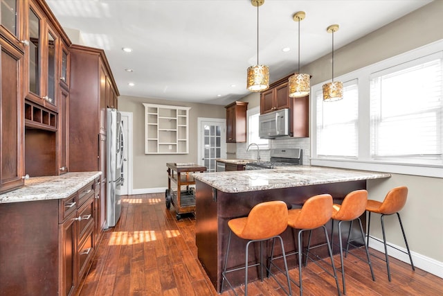 kitchen featuring stainless steel appliances, kitchen peninsula, light stone counters, and decorative light fixtures