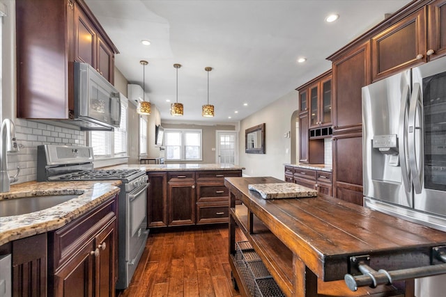 kitchen featuring dark wood-type flooring, decorative light fixtures, stainless steel appliances, light stone countertops, and backsplash