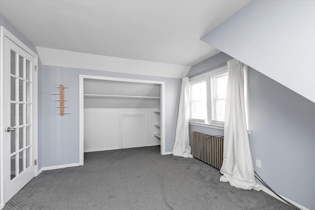 unfurnished bedroom featuring dark colored carpet, vaulted ceiling, radiator, and a closet