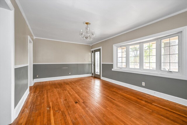 spare room with an inviting chandelier, crown molding, baseboards, and wood finished floors