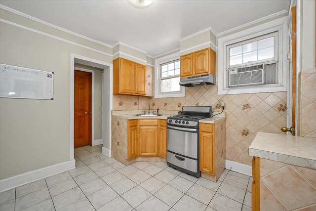 kitchen featuring crown molding, light countertops, light tile patterned flooring, gas range, and under cabinet range hood