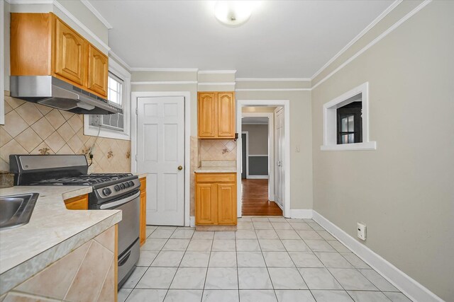 kitchen featuring baseboards, ornamental molding, light countertops, under cabinet range hood, and stainless steel range with gas cooktop