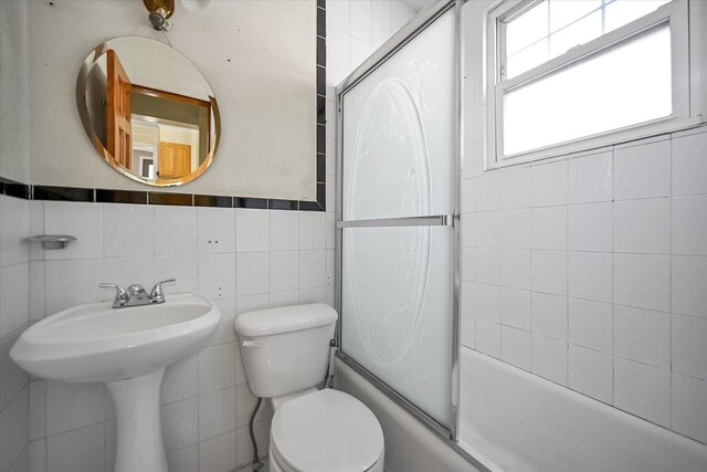 bathroom featuring tile walls, toilet, and bath / shower combo with glass door