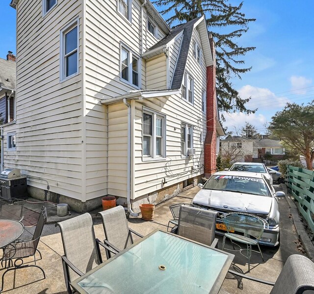 view of side of property featuring outdoor dining area, a patio area, a gambrel roof, and roof with shingles