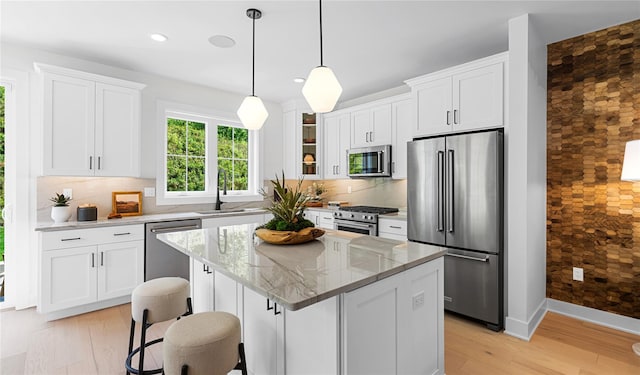 kitchen with a sink, high quality appliances, white cabinets, backsplash, and light stone countertops